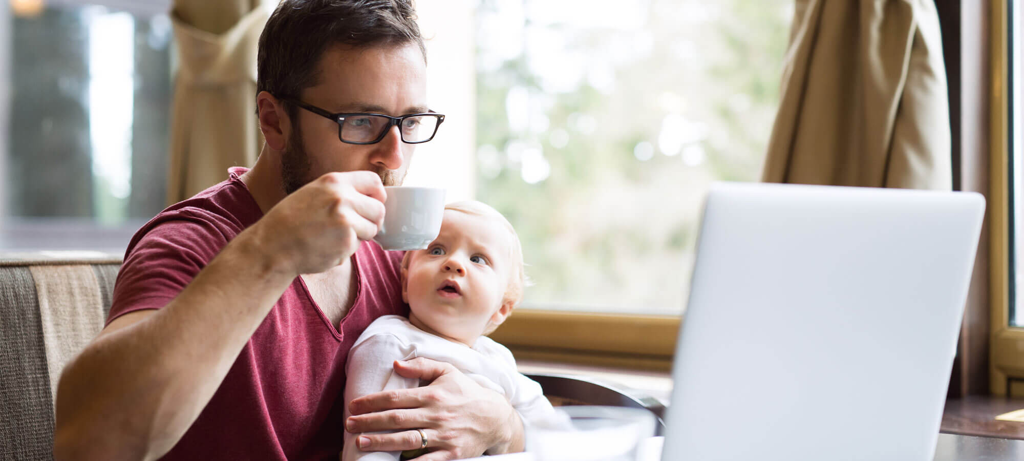 Mann som arbeider på laptop med en baby på fanget